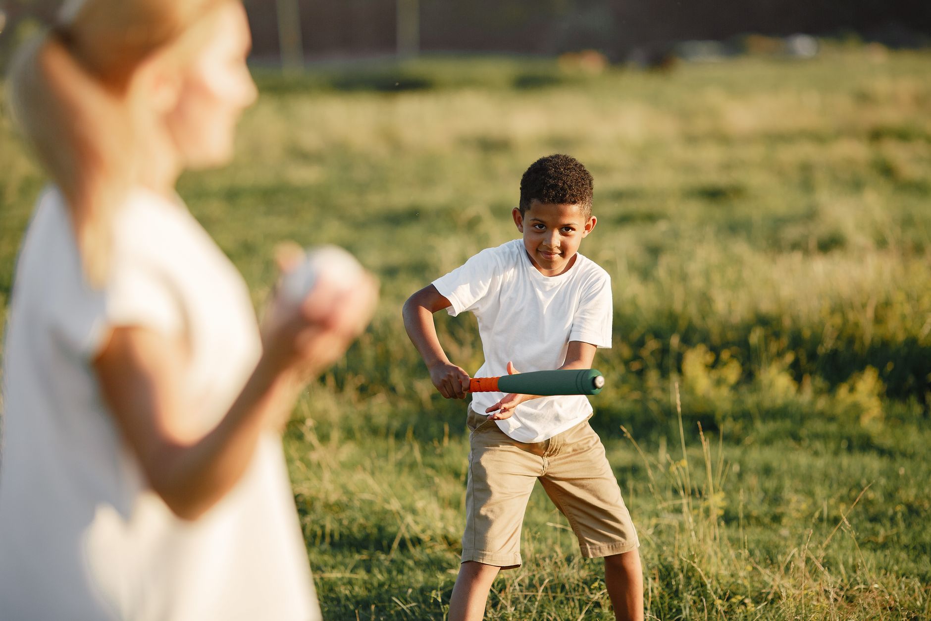 Two kids enjoying a sunny day playing baseball on a grassy field.