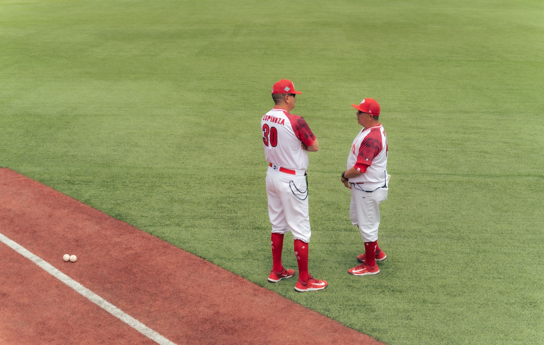 Two baseball coaches in red and white uniforms discussing strategy on the field.