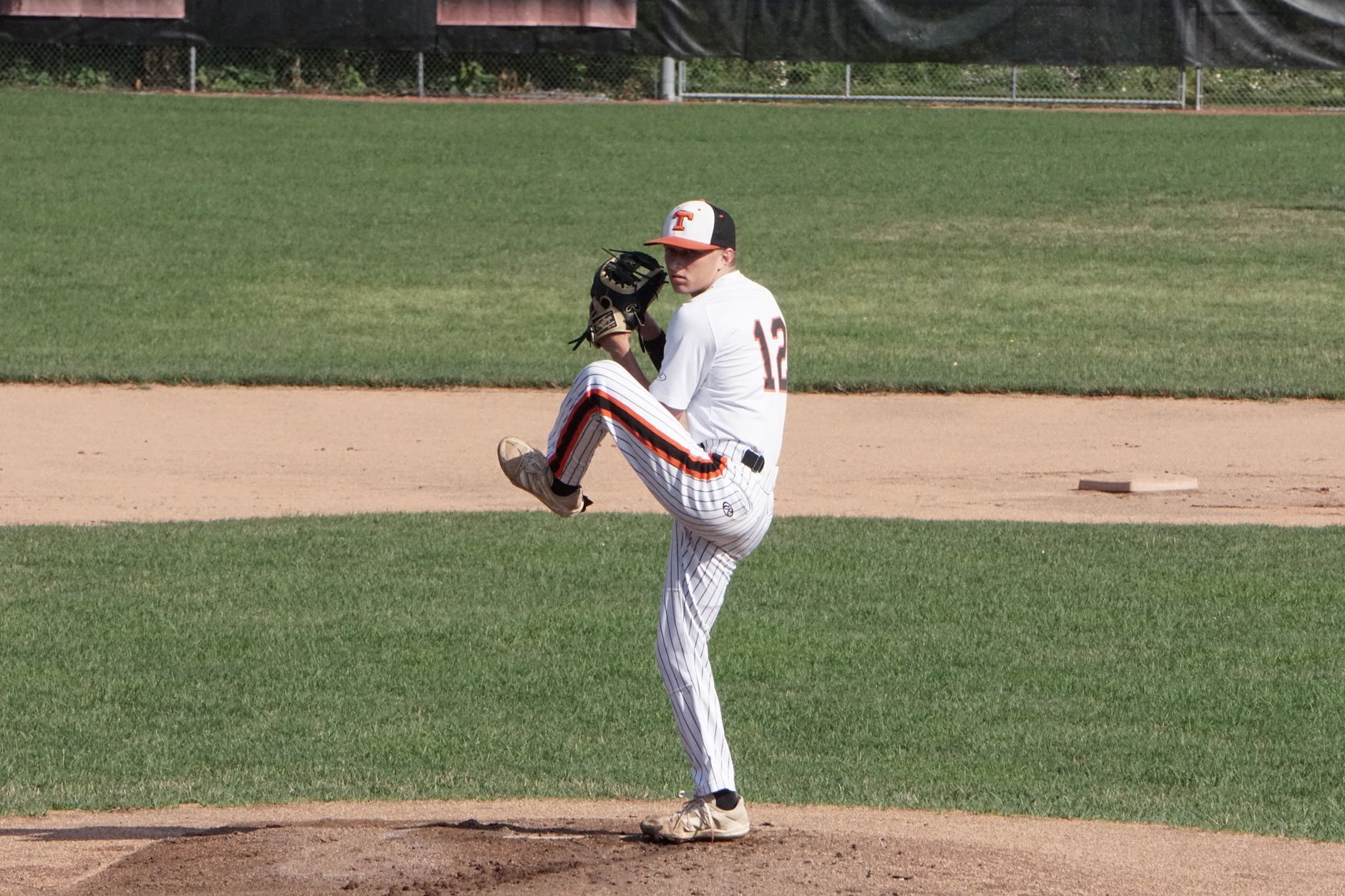 A focused baseball pitcher preparing to pitch during an outdoor game on a sunny day.